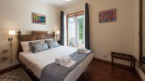 A bedroom with a large bed, a wooden headboard, two wall-mounted lamps, and a view of the outdoors through a sliding glass door. - Heritage Collection House w/ 4BR by LovelyStay (Porto)