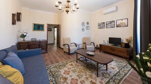 Una sala de estar con un sofá, sillas, una mesa de centro, un televisor y platos decorativos en la pared.