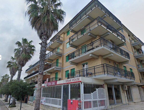 Un edificio de varios pisos con balcones, un restaurante llamado "Passione Carnevale" y palmeras.