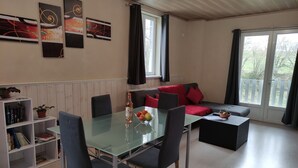Un salon moderne avec une table à manger en verre, des chaises foncées, un canapé rouge et une bibliothèque.