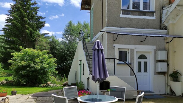 Une terrasse avec une table ronde et quatre chaises, un parasol violet et une porte blanche.
