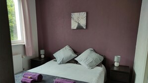 Une chambre à coucher comprenant un lit, deux tables de chevet, une fenêtre avec des rideaux et une œuvre d’art accrochée au mur.