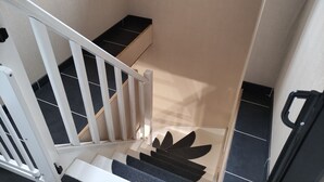 Un escalier avec une rampe blanche et des marches noires, menant à un palier sur lequel se trouve un objet noir.