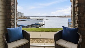 Une vue depuis un balcon, avec des fauteuils en osier, une jetée et un bâtiment situé de l’autre côté de l’eau.