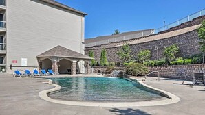 Une piscine avec des chaises longues, un espace salon couvert et un mur en pierre.