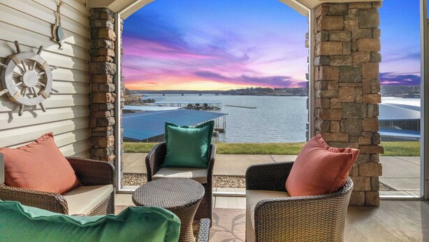 Une terrasse couverte, meublée de mobilier en osier, offrant une vue sur un lac et sur le coucher de soleil.