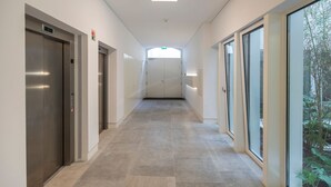 A corridor with elevators, a fire exit, and a large window with a view of greenery. - Hidden Oasis 2BDR Apartment by LovelyStay (Lisboa)