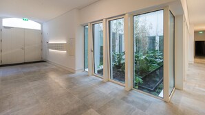 A modern interior with a reception area, large sliding glass doors leading to a garden, and a clean, tiled floor. - Hidden Oasis 2BDR Apartment by LovelyStay (Lisboa)