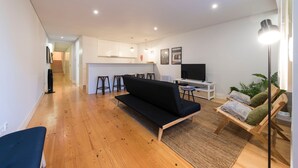 Een moderne woonkamer met een zwarte bank, houten vloer, een klein bijzettafeltje en een televisie.