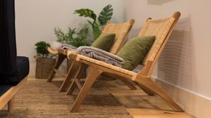 Een rij rieten stoelen met opgevouwen handdoeken en kussens, geplaatst tegen een muur met een plant op de achtergrond.
