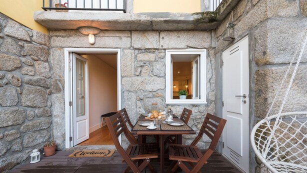 Un espace extérieur aménagé pour les repas, avec des murs en pierre, une table dressée pour deux personnes, des chaises en bois et une petite plante en pot.