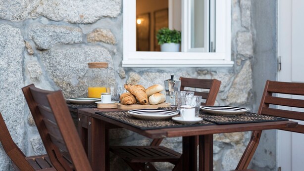 Een stenen muur, een houten tafel en stoelen gedekt voor het ontbijt met croissants, een koffiepot en een glas sinaasappelsap.