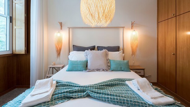 Uma cama bem arrumada com um cobertor verde e branco quadriculado, duas mesas de cabeceira com abajures e um guarda-roupa de madeira.