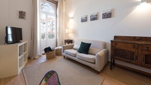 A living room with a sofa, a TV on a stand, a wooden cabinet, and a window with curtains.