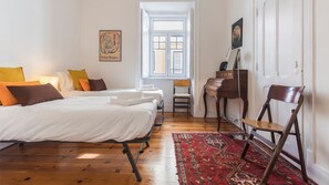 Una camera d'albergo con due letti, una scrivania, una sedia, un tappeto rosso con motivo e una finestra vista.
