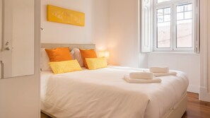 A hotel room with a bed, pillows, a nightstand, a lamp, and a window with a view.