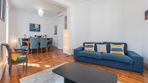 Een woonkamer met een blauwe bank, een eettafel met stoelen en een schilderij aan de muur.