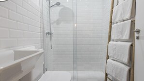Un baño moderno con azulejos blancos tipo metro, una ducha con cerramiento de vidrio, un lavamanos blanco y un perchero con toallas dobladas con cuidado.