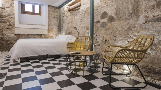 Una habitación con una cama, dos sillas de mimbre, una mesita y un suelo a cuadros.