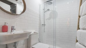 A modern bathroom with a white sink, a glass shower enclosure, and a toilet.