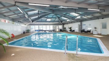 Una piscina interior con estructura en el techo, un flotador salvavidas y una pared con señal de salida de incendios.