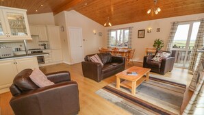 A spacious living area with a dining table, two sofas, a coffee table, and a kitchen in the background. - Lodge 23 (Torpoint)