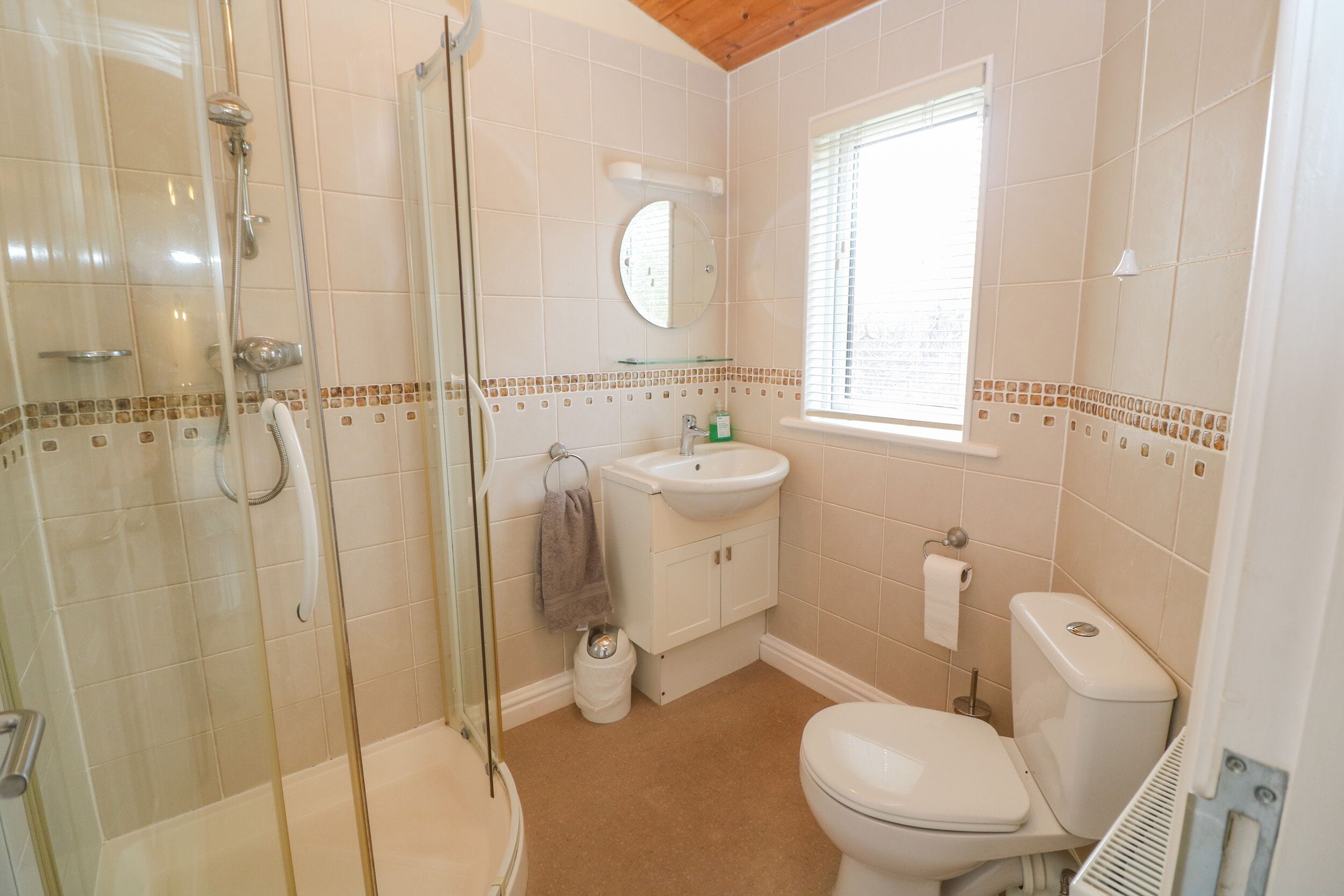 A bathroom with a glass-enclosed shower, a sink, a toilet, and a window with blinds.