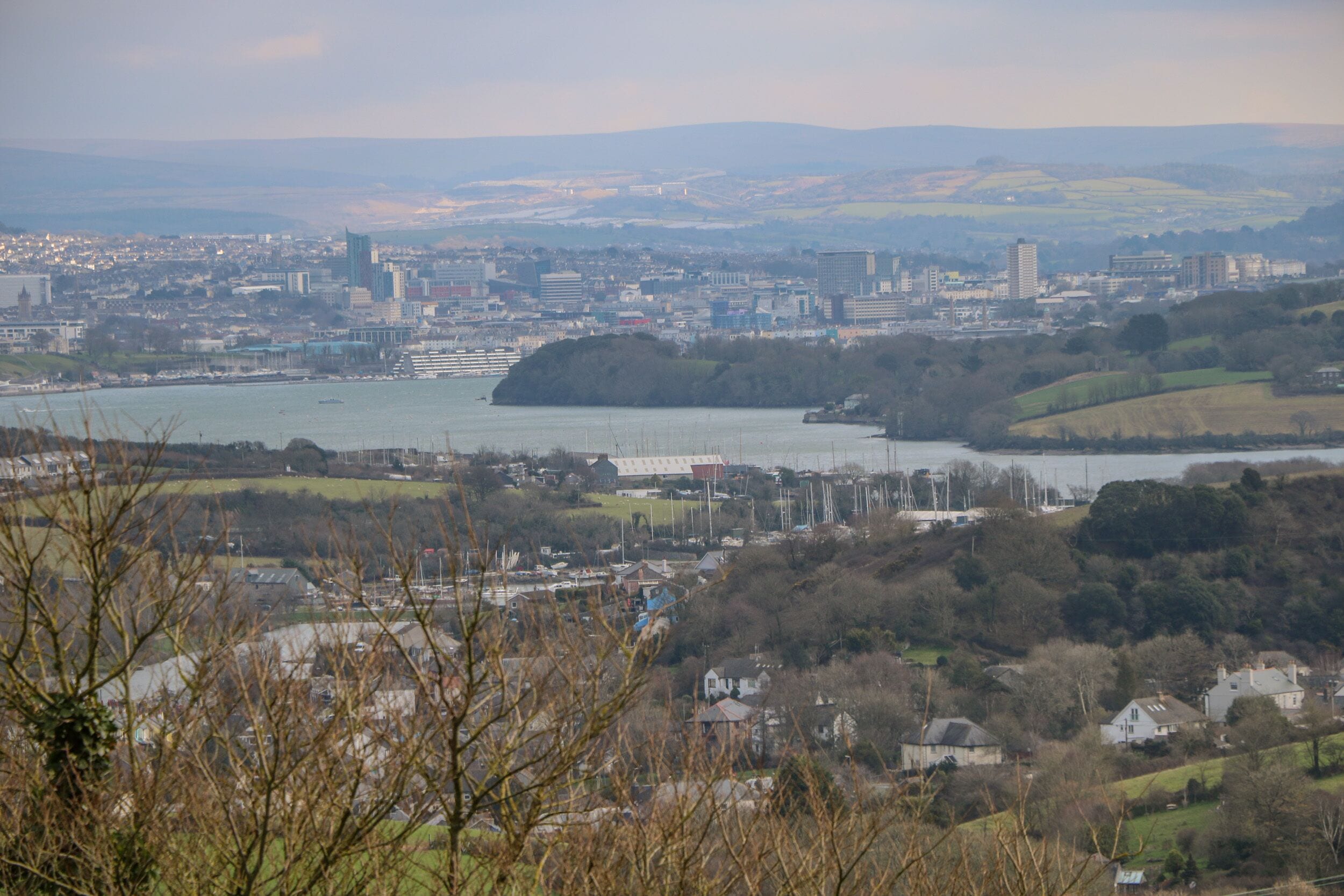 A panoramic view of a coastal city with a river, hills, and a mix of residential and commercial buildings.