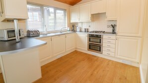 A modern kitchen with white cabinets, a wooden floor, a microwave, a stove, and a sink. - Lodge 23 (Torpoint)