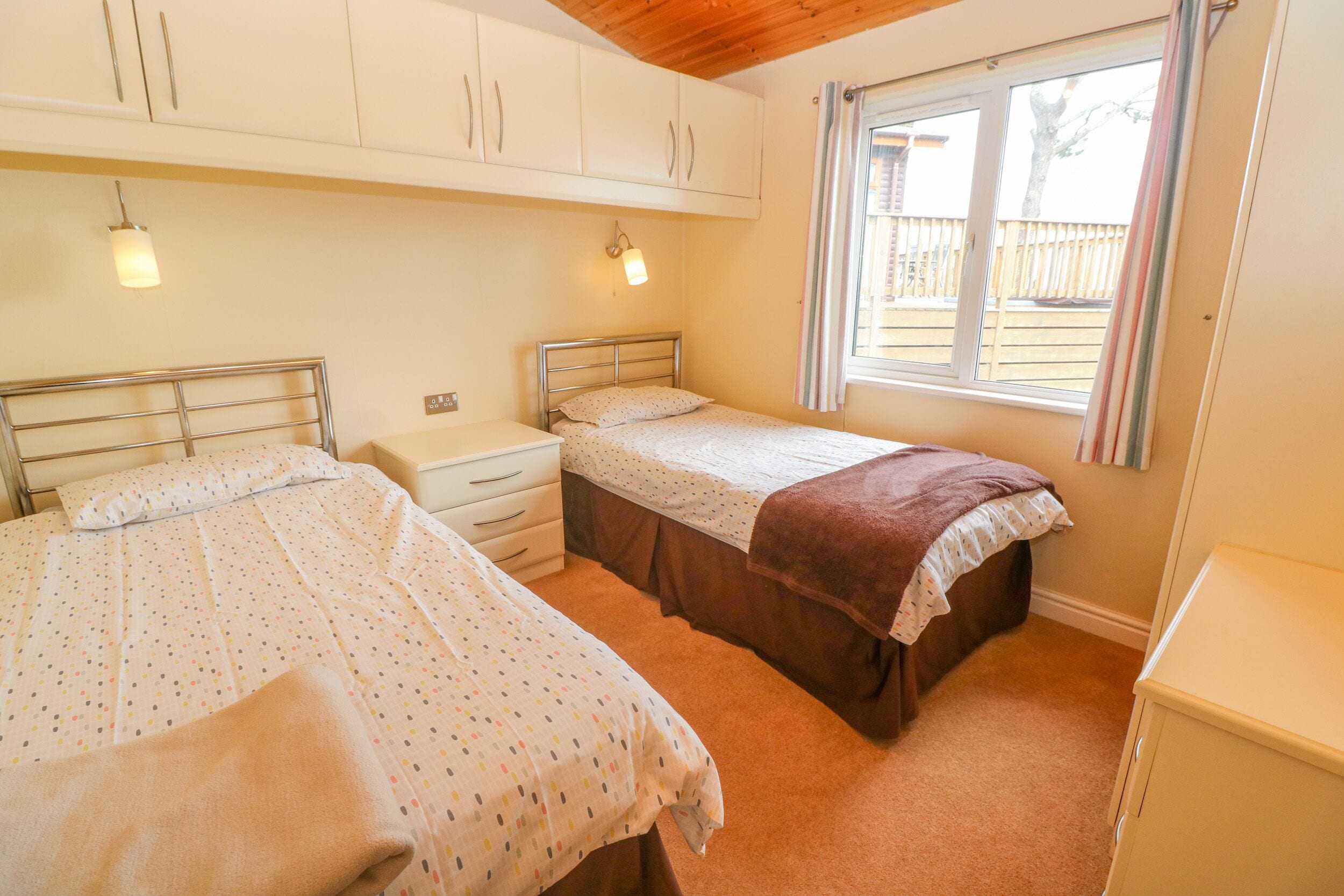 A bedroom with two beds, a window with curtains, and a wooden ceiling.