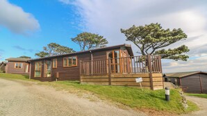 A row of wooden cabins with large windows and a grassy area in front. - Lodge 23 (Torpoint)