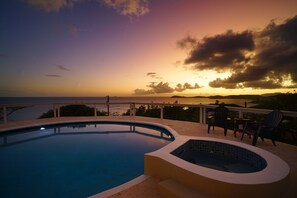 Piscina con jacuzzi y zona de estar exterior, con vistas a un hermoso atardecer.