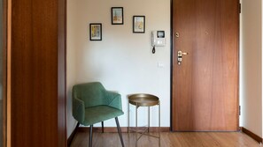 A room with a wooden door, a green chair, a small round table, and two framed pictures on the wall.