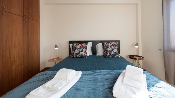 A neatly made bed with blue bedding, two white towels, and floral-patterned pillows.