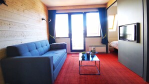 A room with a blue sofa, a red carpet, a small table with a vase and a candle, and a TV mounted on the wall. - NEW - ULTRA CENTER & PANORAMIC VIEW (Huez)