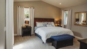 Une chambre à coucher avec un grand lit, des lampes de chevet, un banc et un miroir au mur.