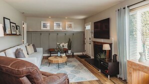 Una sala de estar con sofá, mesa de centro, chimenea y televisor montado en la pared.