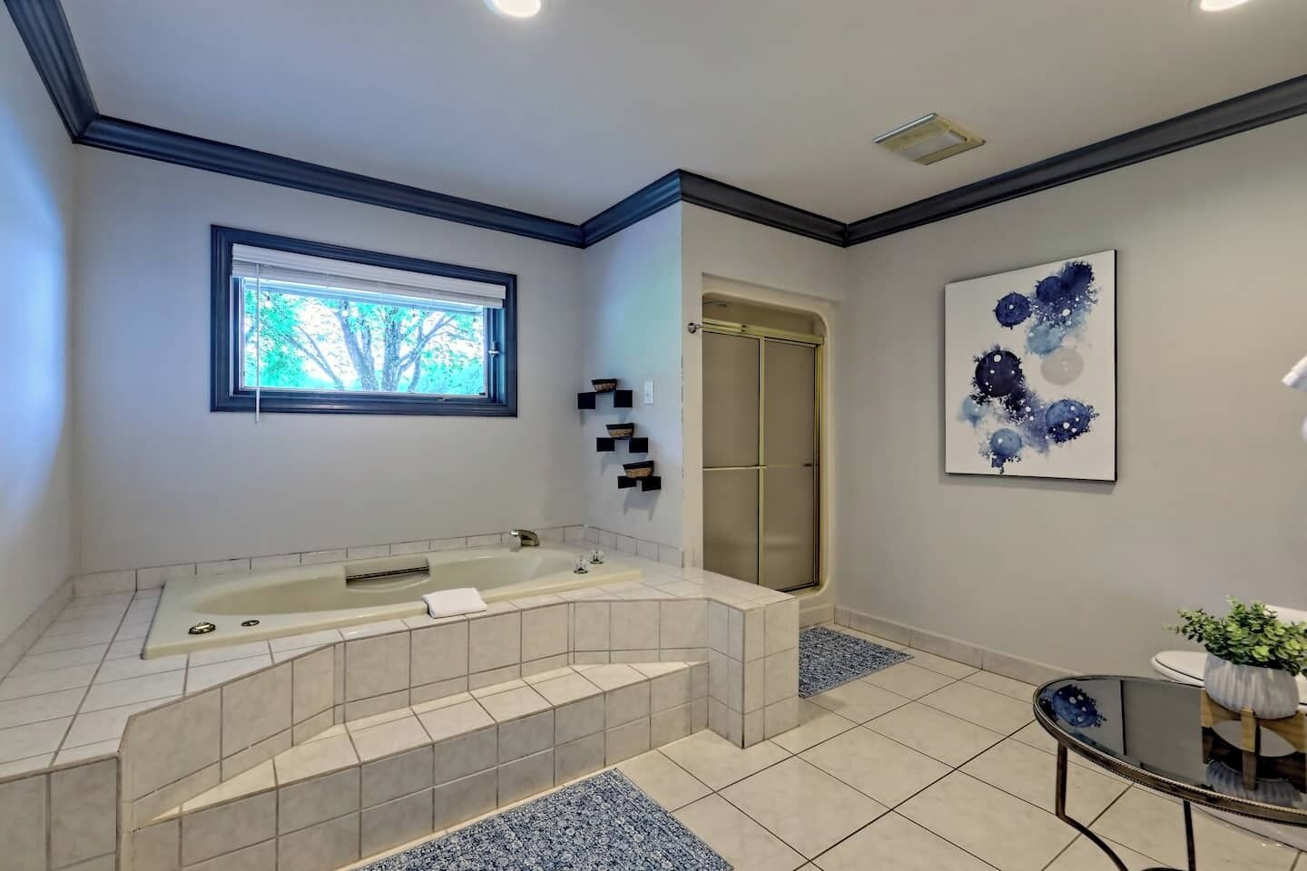 A bathroom with a large bathtub, a walk-in shower, a window, and a framed abstract painting.
