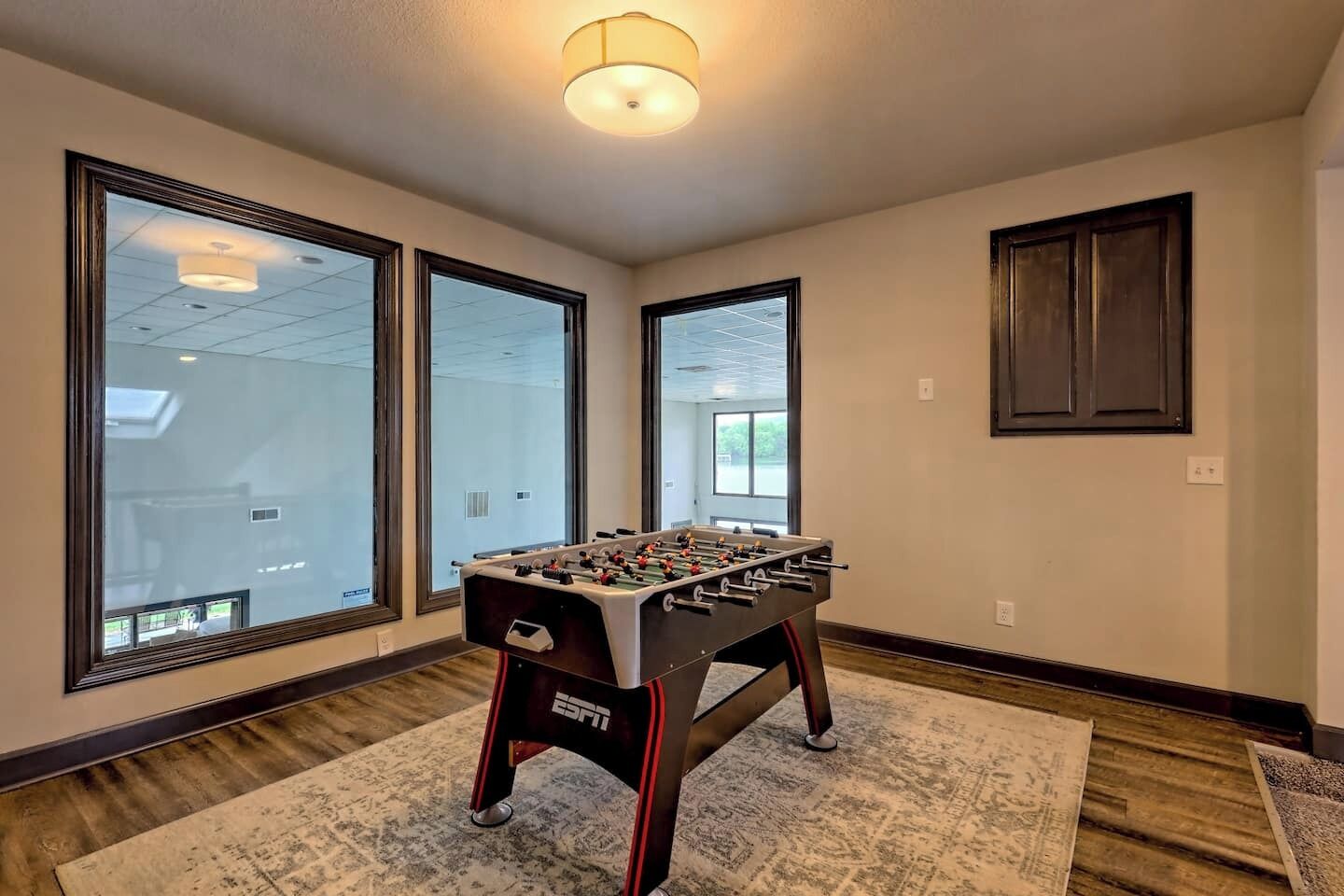 Quarto com mesa de futebol de mesa, janelas amplas e piso de madeira.