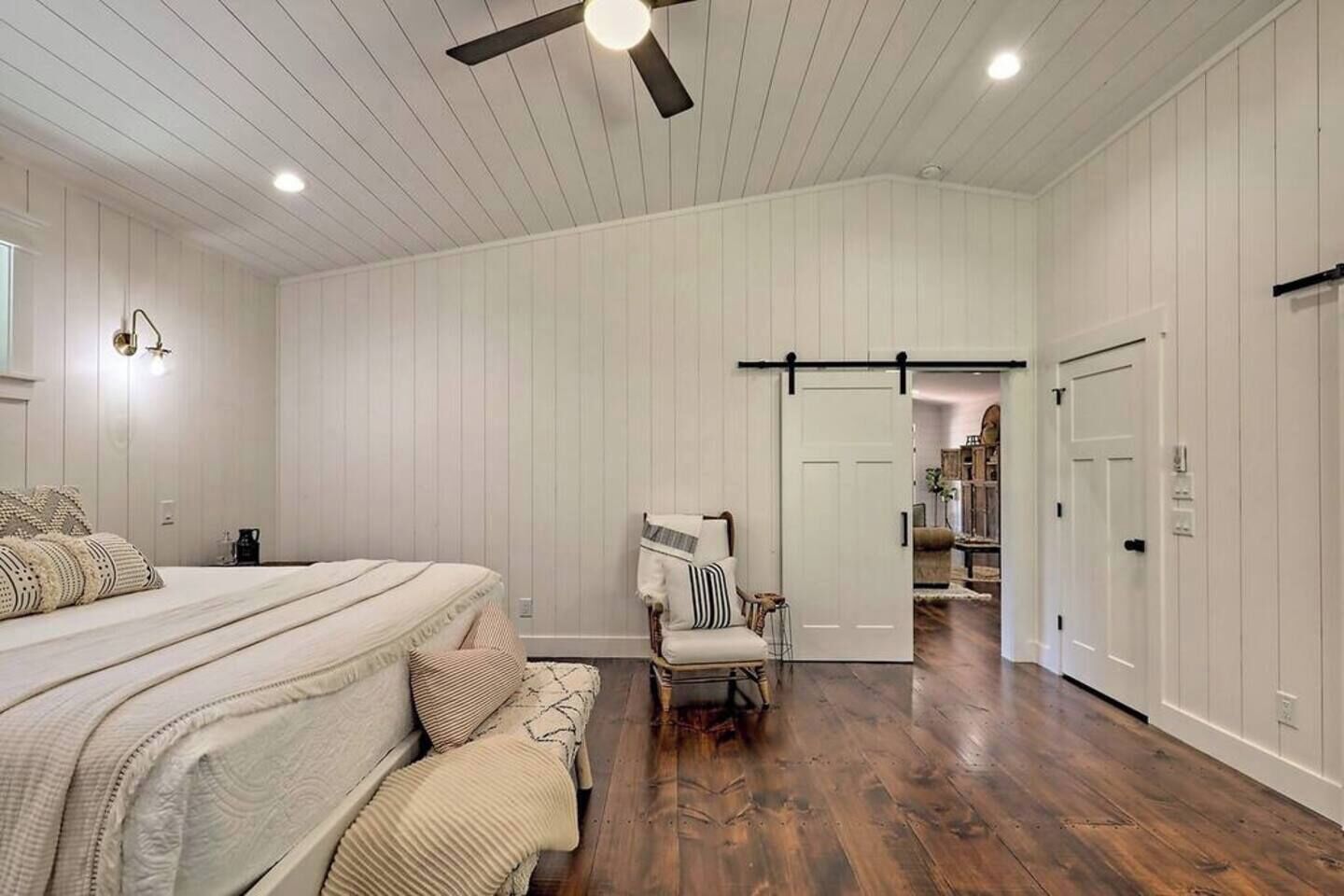 Un dormitorio con cama, una silla, un armario y una puerta que da a otra habitación.