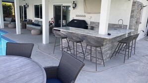 Un patio al aire libre con barra, asientos y piscina.