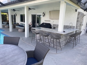 An outdoor patio with a bar area, seating, and a pool.
