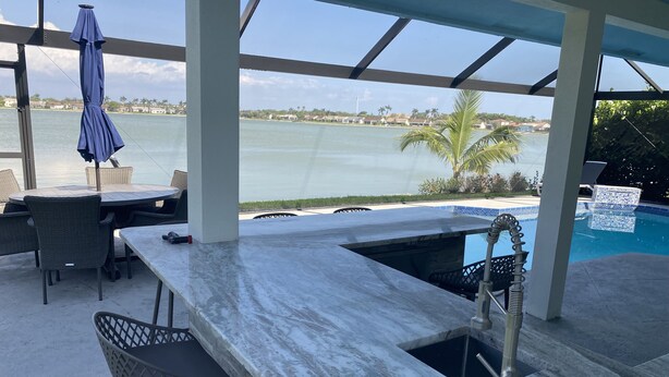 Zona de bar al aire libre techada, con piscina, taburetes de bar y vistas al agua.