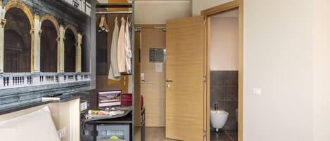 A hotel room with a bed, a desk with a computer, a wardrobe, and a bathroom with a toilet and sink.