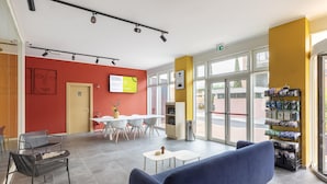 A modern interior with a blue sofa, a dining area with white chairs, and a vending machine. - B&B Hotel Roma Fiumicino Aeroporto Fiera 2 (Fiumicino)
