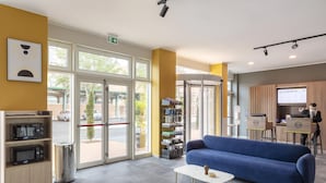 A reception area with a blue sofa, a white coffee table, a bookshelf, and a trash bin. - B&B Hotel Roma Fiumicino Aeroporto Fiera 2 (Fiumicino)