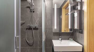 Une salle de bain moderne dotée d’une douche à parois de verre, d’un lavabo blanc et d’un miroir avec éclairage intégré.
