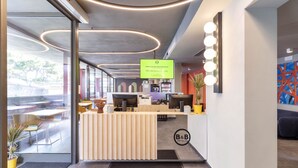 A modern hotel reception area with a wooden reception desk, computers, and a green sign.