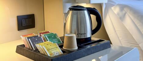 A hotel room with a Tognana electric kettle, a tray with tea bags, and a cup.