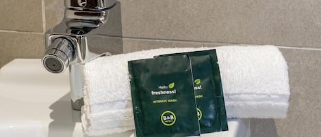 A bathroom sink with a towel dispenser holding a green package labeled 'Hello Freshness! Intimate Wash' from B&B Hotels.